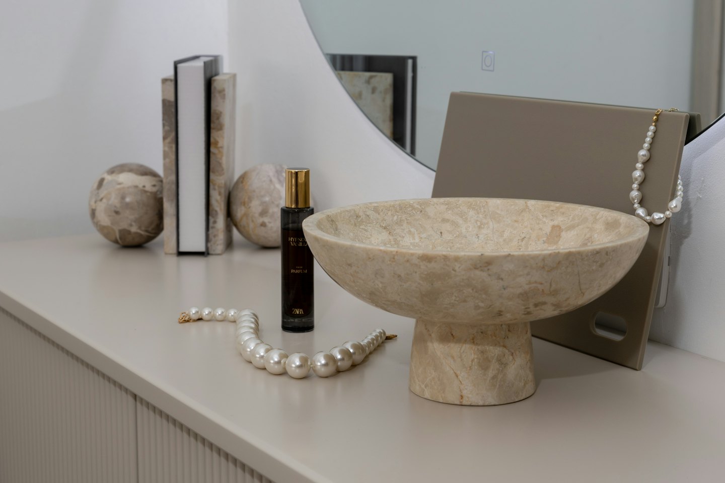 Elegante tocador con cuenco de mármol, perfume y collares de perlas.